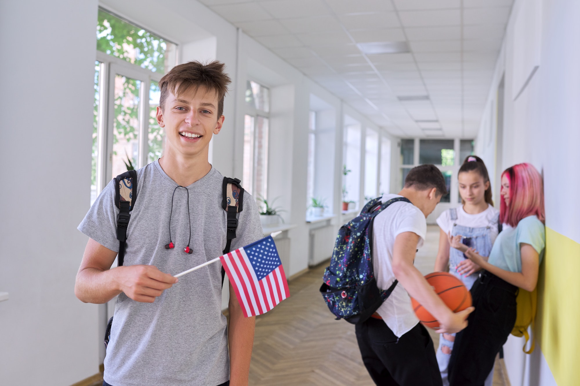 Male student teenager with USA flag inside college, group of students background